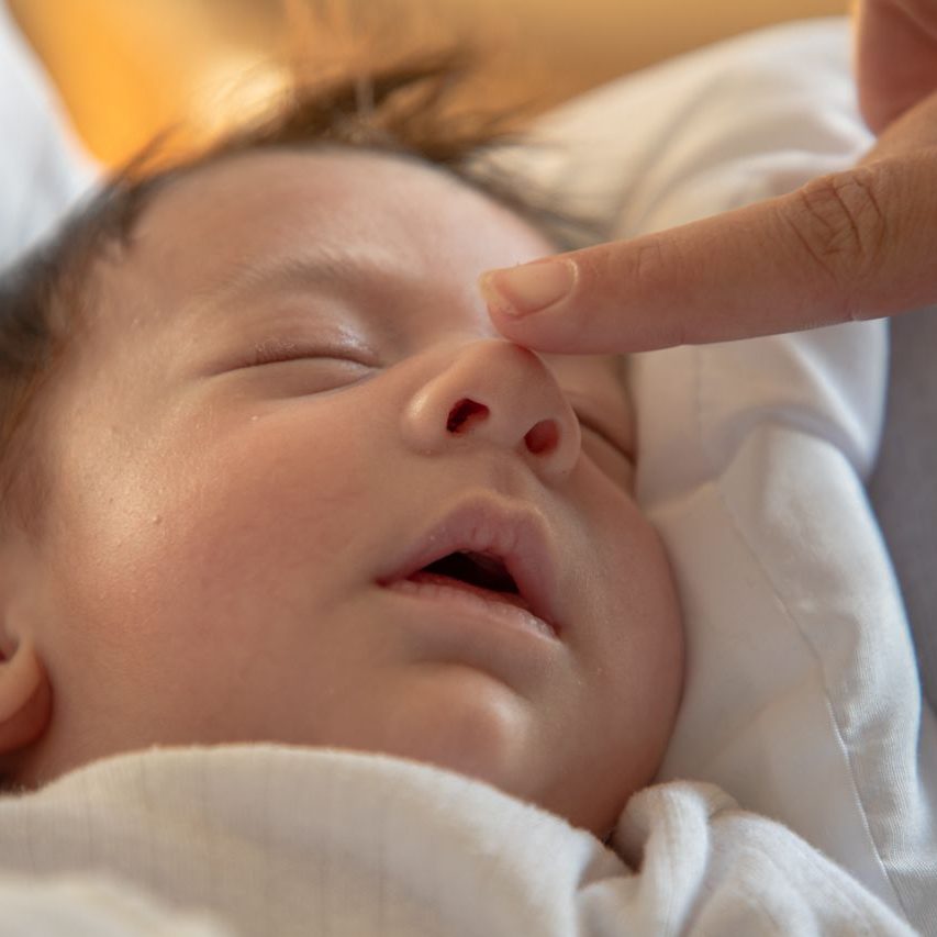 A tender moment capturing a sleeping baby with a finger gently touching the nose.