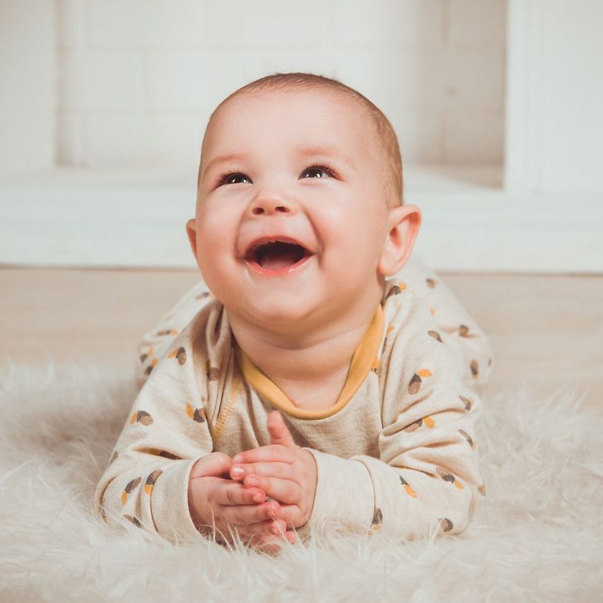 Joyful baby lying on a fluffy rug, smiling and looking upwards indoors.