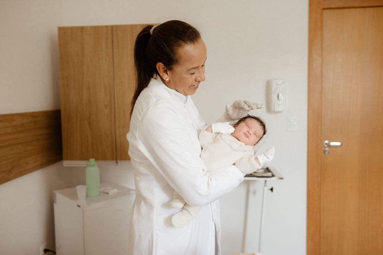 A medical practitioner gently holding a newborn baby in a hospital room, symbolizing care and health.