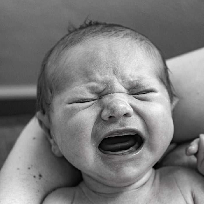 Close-up black and white photograph of a crying newborn being cradled in arms.