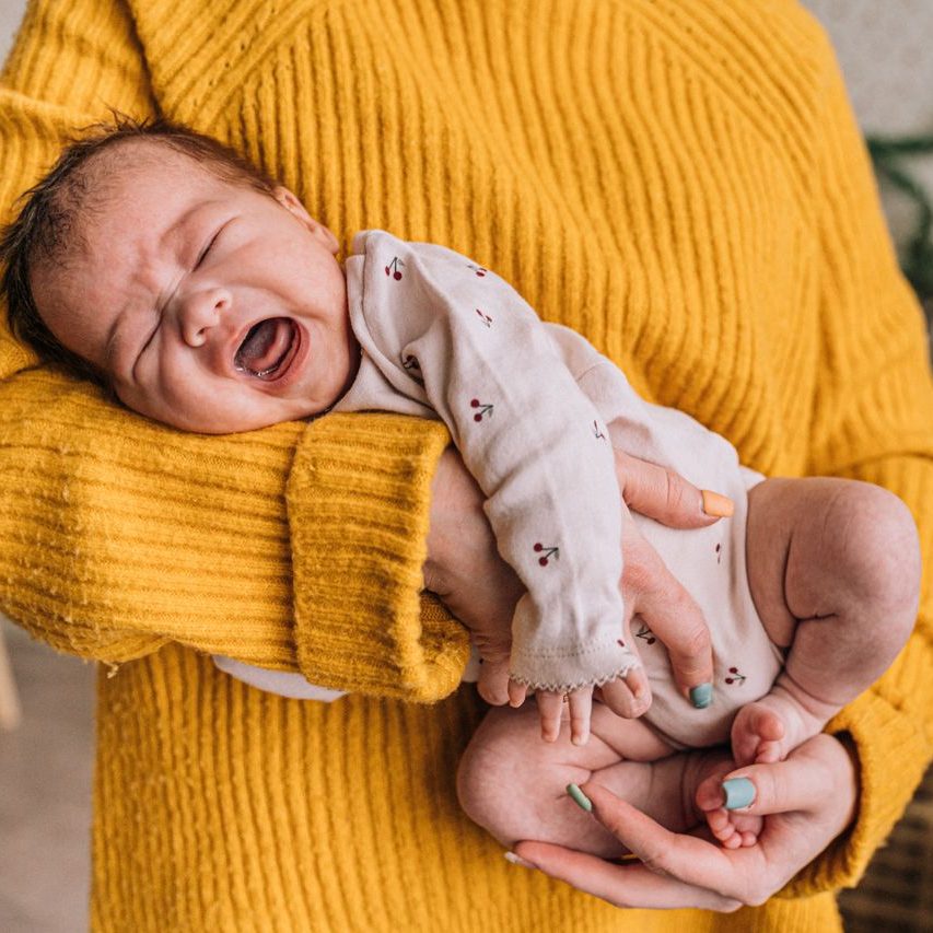 A mother gently holds a crying baby in her arms, providing warmth and comfort indoors.
